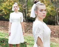 a woman wearing a white dress and headpiece standing in the grass with trees behind her