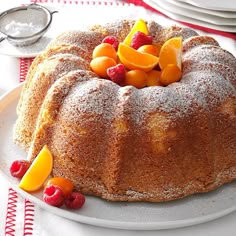 a bundt cake on a plate with fruit and powdered sugar around the edges