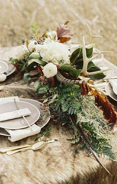 the table is set with plates, silverware and floral centerpieces on it