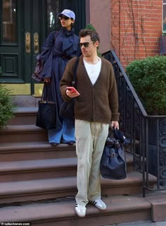 the man is walking down the steps with his handbag and cell phone in his other hand