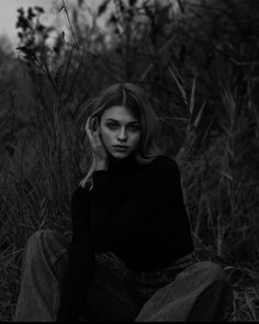 a black and white photo of a woman sitting in the grass with her hand on her face