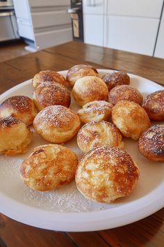 a white plate topped with lots of powdered sugar covered donuts on top of a wooden table