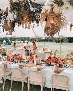 a group of people standing around a table covered in white cloths and chairs under a tent