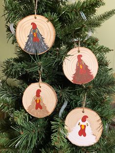 three wooden ornaments are hanging from a christmas tree with pine needles and painted roosters on them