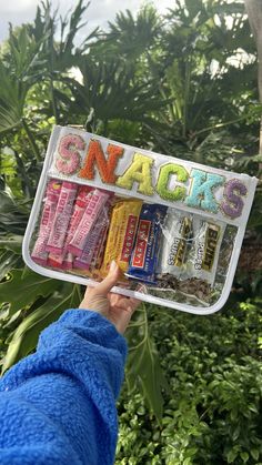 someone holding up a package of snacks in front of some trees