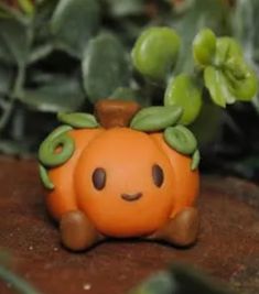 an orange toy sitting on top of a wooden table next to green leaves and plants