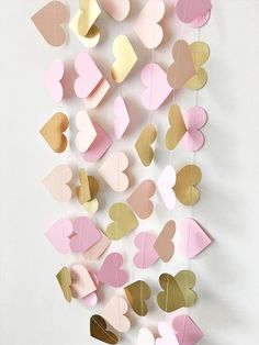 pink, gold and white hearts hanging from strings on the wall in front of a white background