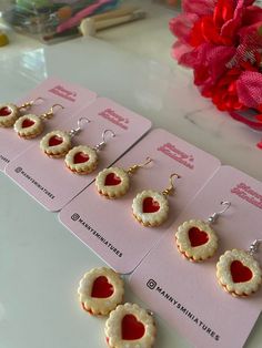 four pairs of heart shaped cookies are displayed on pink cards with red flowers in the background