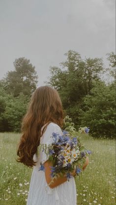 a girl in a white dress holding a bouquet of wildflowers and daisies