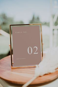 a table number sitting on top of a wooden plate next to a white bird feather