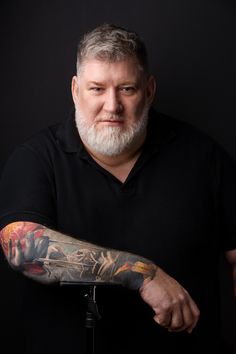 a man with tattoos on his arm and arms is standing in front of a black background