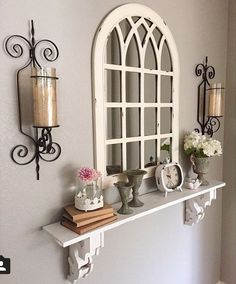 a shelf with candles, vases and flowers on it in front of a window