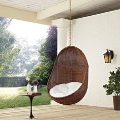 a brown hanging chair on a porch next to a table