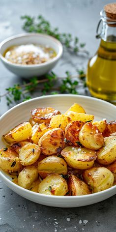 a white bowl filled with cooked potatoes next to a bottle of oil and seasoning