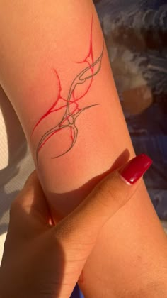 a woman's arm with a red and silver tattoo design on her left arm