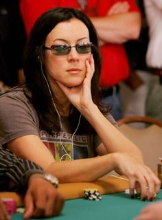 a woman sitting at a poker table with her hand on her chin and headphones to her ear