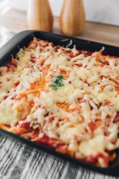 a square casserole dish with cheese and sauce on the top, next to two wooden utensils