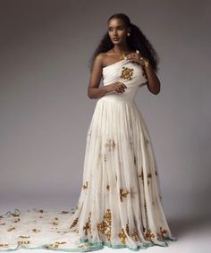 an african woman in a white dress with gold flowers on the skirt and one shoulder