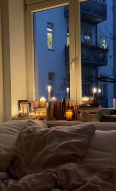 candles are lit in front of a window with an unmade bed next to it