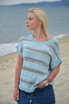 a woman is standing on the beach wearing a blue and gray sweater with sequins