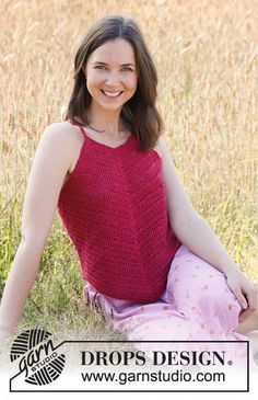 a woman sitting in the grass with her legs crossed and wearing a red tank top