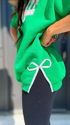 a woman wearing a green sweatshirt and black leggings with a bow on the side