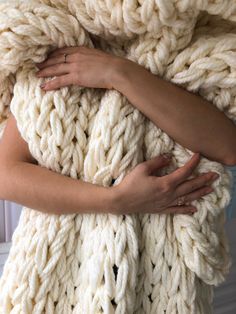 a woman wrapped in a chunky blanket with her hands on the top of it