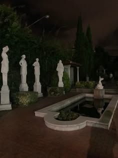 the statues are all lined up in front of the water fountain at night, with lights shining on them