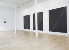 three black and white paintings hanging on the wall in an empty room with wooden floors