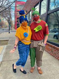 two people in costumes standing next to each other on the sidewalk near a store front