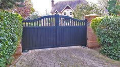 a gated driveway with brick pavers leading to a house in the back ground