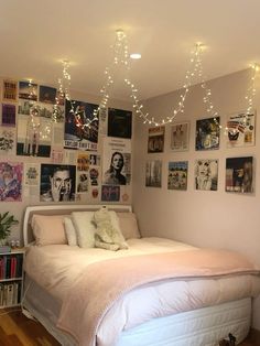 a white bed sitting in a bedroom next to a wall with pictures on it and lights hanging from the ceiling