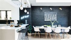 a black brick wall in a modern kitchen with white chairs and counter tops, along with an island