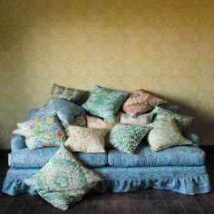 a pile of pillows sitting on top of a blue couch in front of a yellow wall