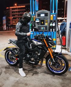 a man in black jacket sitting on motorcycle at gas station with gas pump and fuel dispenser