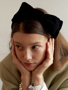 a woman with a black bow on her head is looking at the camera while she holds her hand near her face