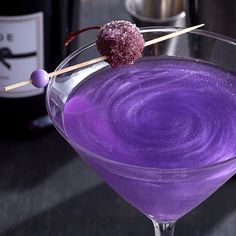 a purple drink in a wine glass with a stick sticking out of the rim and some sugar on top