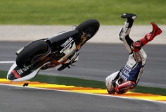 a person on a motorcycle falling off the side of a race track while another person holds their hand up in the air