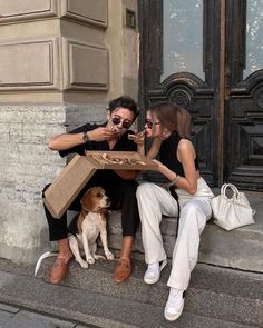 two people sitting on the steps eating pizza with a dog looking at their cell phones