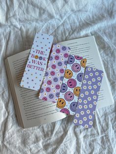 three bookmarks sitting on top of an open book next to each other with smiley faces