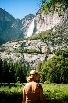 a woman standing in front of a mountain with a waterfall coming out of the side