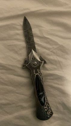 a knife that is laying on top of a white bed sheet with an intricate design