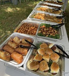 many trays of food are lined up on a long table in the grass outside