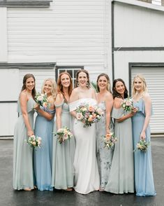 a group of women standing next to each other in front of a white building holding bouquets