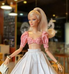 a barbie doll with blonde hair wearing a white skirt and pink top holding a purse