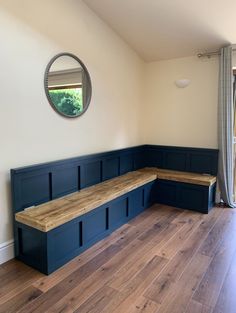 a room with wooden floors and blue painted benches on the wall, along with a round mirror