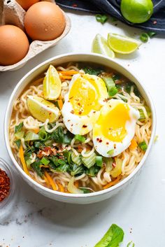 a bowl filled with noodles and eggs on top of a white table next to some ingredients