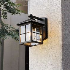 a light that is attached to the side of a building with trees in front of it