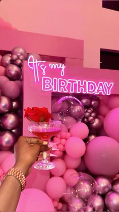 a person holding a wine glass in front of a pink birthday backdrop with balloons and balls