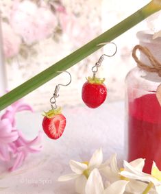 two strawberries dangling from earrings next to flowers